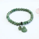 Cyan jade laughing Buddha bracelet with smooth round jade beads and hand-carved Buddha pendant on elastic string, flat lay view