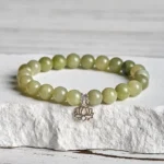 Cyan jade lotus charm bracelet with sterling silver pendant displayed on white textured stone surface, handmade jade beads
