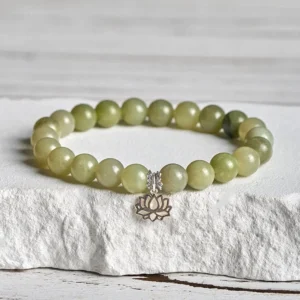 Cyan jade lotus charm bracelet with sterling silver pendant displayed on white textured stone surface, handmade jade beads