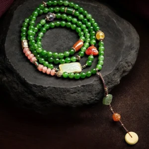 Overhead view of 108 cyan jade mala beads bracelet with laughing Buddha red agate head and hetian jade ruyi charm displayed on dark stone