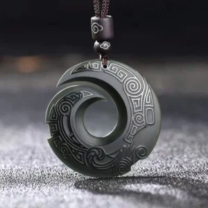 Handcrafted cyan jade peace buckle showing engraved geometric and spiral patterns, top-down studio shot