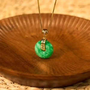 Cyan jade peace buckle necklace displayed on wooden bowl with woven rattan mat, showing natural green jade pendant with gold clasp detail