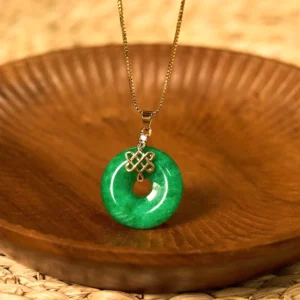 Handcrafted cyan jade peace buckle necklace displayed on wooden tray with woven rattan mat background, showcasing the authentic jade pendant with gold chain and traditional Chinese knot detail