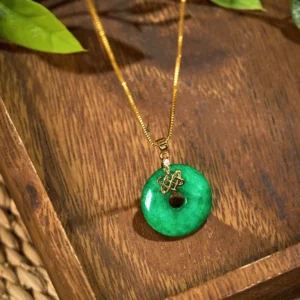 Polished cyan jade peace buckle pendant necklace photographed with natural lighting and green foliage, highlighting the translucent quality and vibrant green coloring of premium natural jade stone