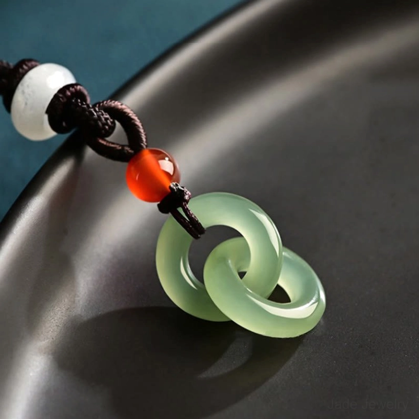 Side oblique view of cyan jade double ring pendant on black ceramic showing smooth polished jade surface