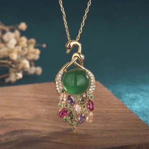Cyan jade peacock pendant necklace with gold chain and multi-color gemstone inlay, front view on wooden display