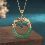 Natural cyan jade round pendant necklace with gold filigree setting and pink gemstone accents on wooden display