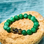 Cyan jade Pixiu wealth bracelet with gold enamel charm overhead flat lay on natural stone with water backdrop