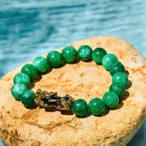 Cyan jade Pixiu wealth bracelet with gold enamel charm overhead flat lay on natural stone with water backdrop