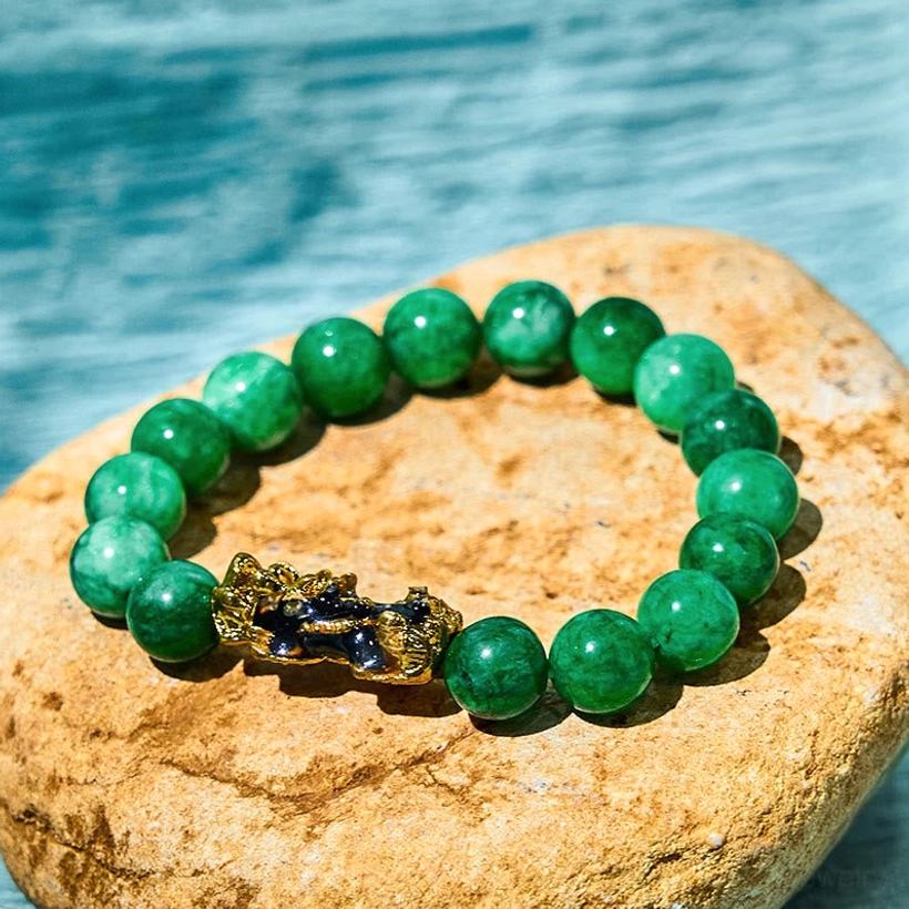 Cyan jade Pixiu wealth bracelet with gold enamel charm overhead flat lay on natural stone with water backdrop