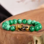 Cyan jade pixiu wealth bracelet with gold-black enamel charm on wooden display, top-down view