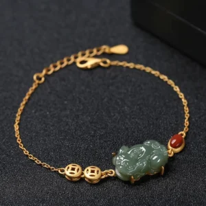 Cyan jade pixiu wealth bracelet with red agate beads and gold-plated copper coin charm on dark tabletop
