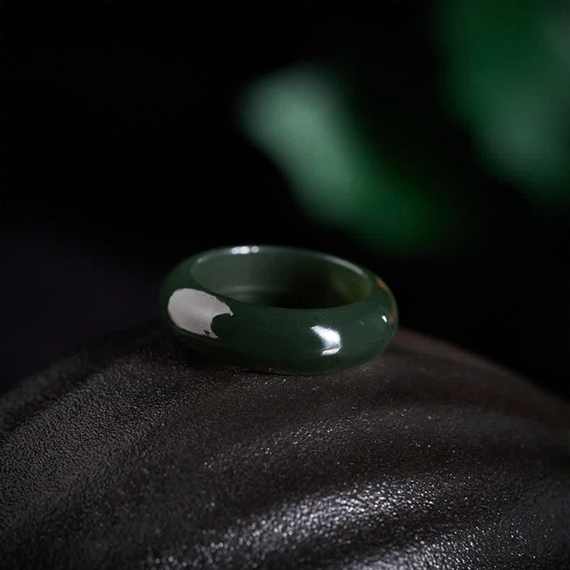 Glossy deep green cyan jade seamless band ring on black leather fabric, oblique overhead view