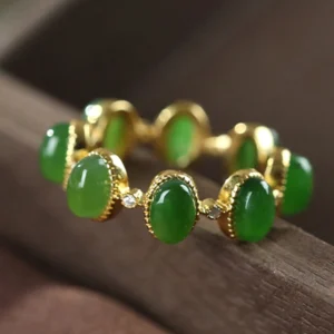 Adjustable jade ring close-up side perspective showing delicate gold bezels and clear spacer stones, dark wooden background