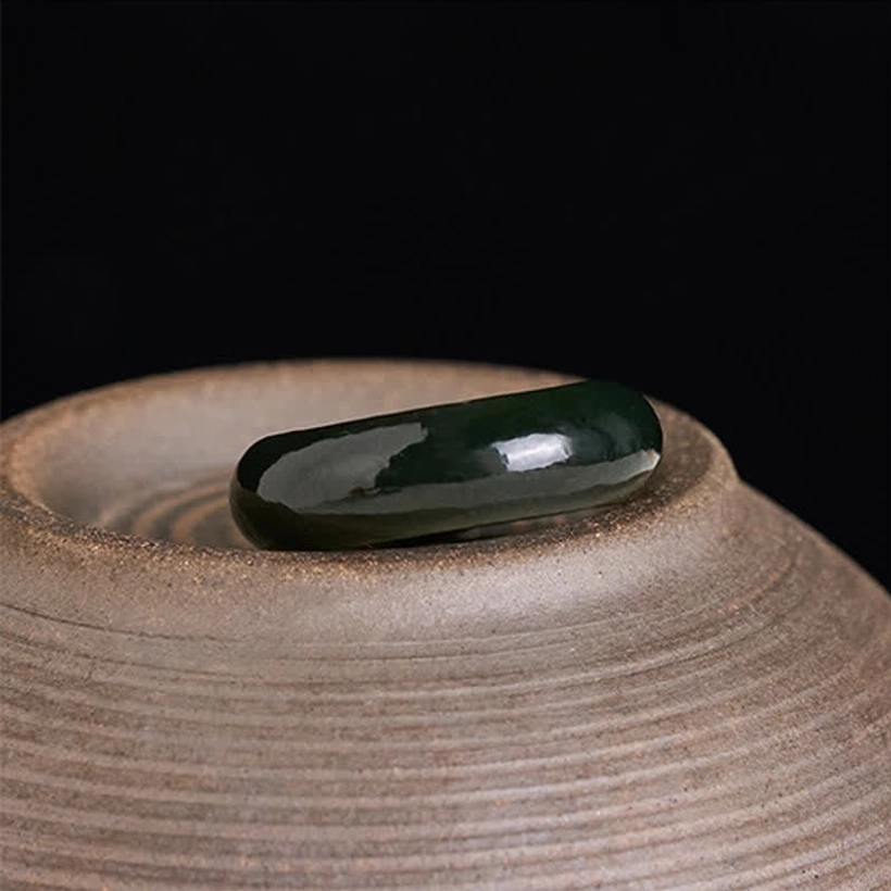 Natural cyan jade band ring viewed from top-down side angle on unglazed ceramic, minimalist solid design