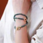 Cyan jade triple wrap bracelet with peace buckle charm and gold-plated sterling silver, styled on wrist with formal attire showing side view of the stacked jade beads and pendant tassel