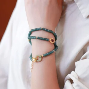 Cyan jade triple wrap bracelet with peace buckle charm and gold-plated sterling silver, styled on wrist with formal attire showing side view of the stacked jade beads and pendant tassel
