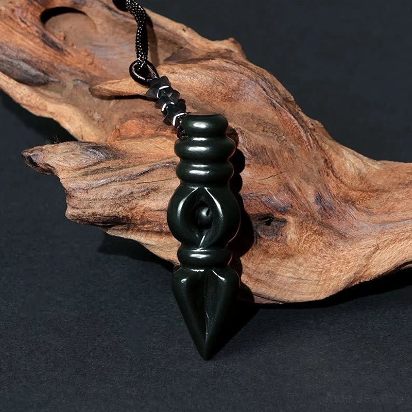 Vajra Dorje pendant from three-quarter angle showing carved circular details, pointed tip, and hand-woven black suspension cord