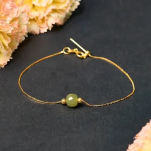 Dark green natural jade bead bracelet with 925 sterling silver chain, flat lay view with pink floral styling