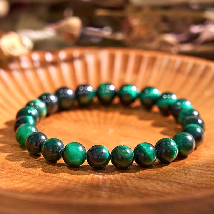 Dark green tiger eye jade balance bracelet flat lay on wooden surface, polished round beads showing deep forest green and brown striped pattern