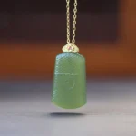 Dark green Hetian jade Om pendant necklace with engraved sacred symbol and 925 sterling silver bail, front view on wooden table