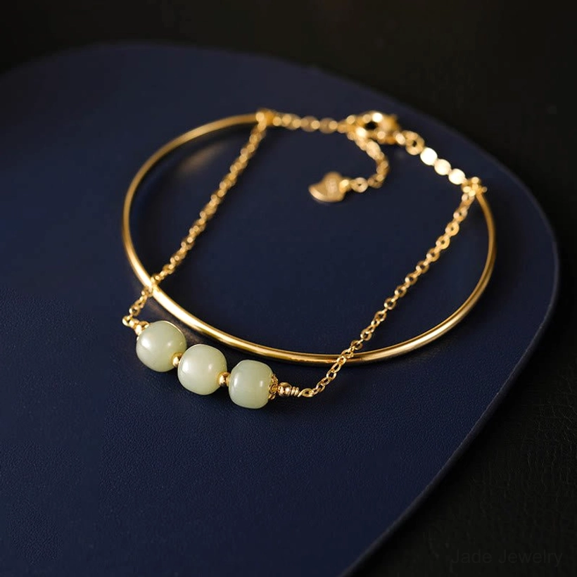 Close up side view of double layer jade bangle bracelet with open gold plated design and jade beads on dark blue tray