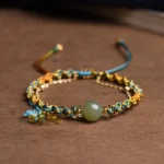 Handmade double layer jade prosperity bracelet with blue and yellow braided rope and jade bead, overhead view on wooden surface