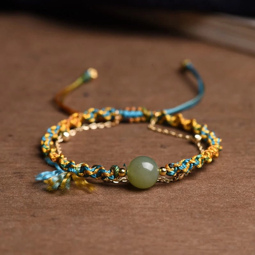 Handmade double layer jade prosperity bracelet with blue and yellow braided rope and jade bead, overhead view on wooden surface
