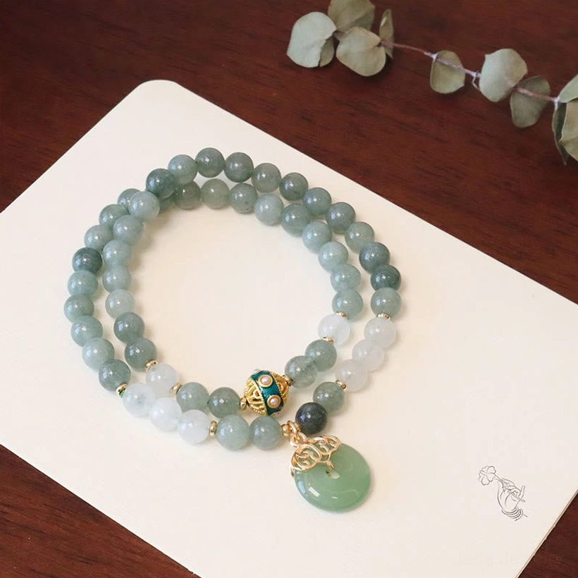 Double layer jade peace buckle bracelet with two-tone jade beads and gold metal accents with eucalyptus decor on dark wood