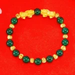 Gold-plated double Pixiu green agate wealth bracelet overhead view, natural jade beads with gold spacer accents on red background