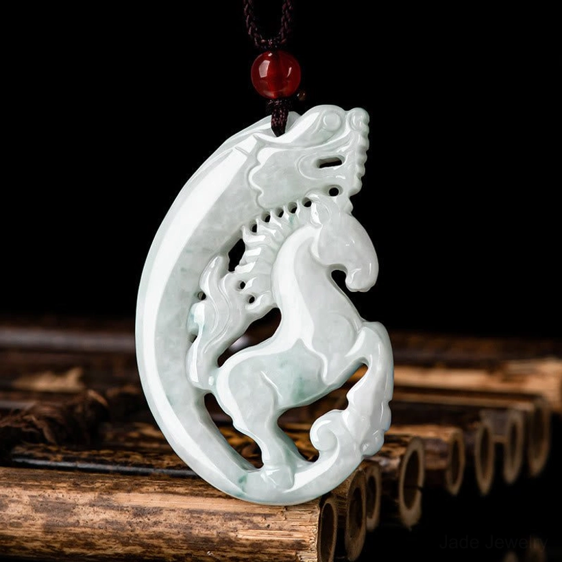 Right three-quarter view of carved jade dragon horse pendant with green veins, brown necklace cord and decorative red bead on dark background