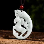 Dragon horse jade pendant necklace carved with intricate hollow design, displayed on wooden stand with brown rope cord and red bead