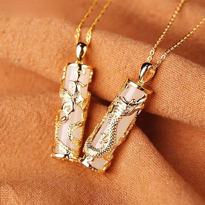 Dragon and phoenix jade pendants pair with polished gold copper setting on fabric background, showing fine hand-carved details
