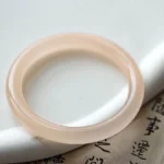 Dusty rose pink jade bangle close-up top view, solid thin round polished jade band on calligraphy paper