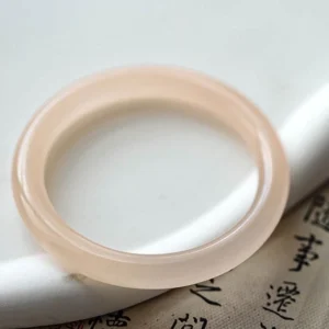 Dusty rose pink jade bangle close-up top view, solid thin round polished jade band on calligraphy paper