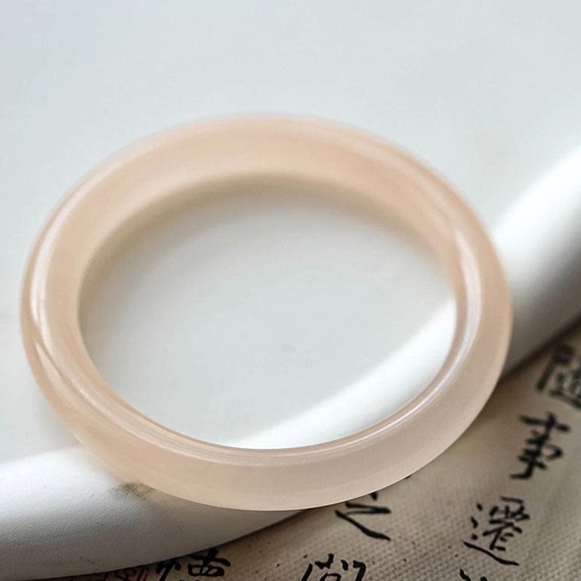 Dusty rose pink jade bangle close-up top view, solid thin round polished jade band on calligraphy paper