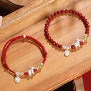 Fire Horse cinnabar jade red string bracelet pair with sterling silver charm and blessing engraved tag on wooden surface