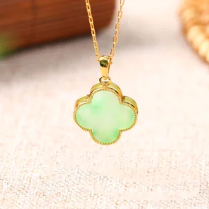 Natural light green jade four leaf clover pendant direct front view with gold-plated metal frame on wooden table