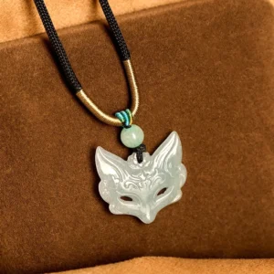 Fox mask jade pendant necklace with black-gold woven rope, light green carved jade fox, overhead front view on brown fabric