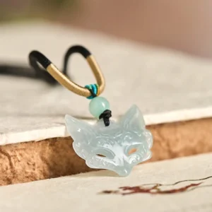 Adjustable fox mask jade pendant necklace showing rope loop closure and carved jade detail, side oblique view on wooden surface