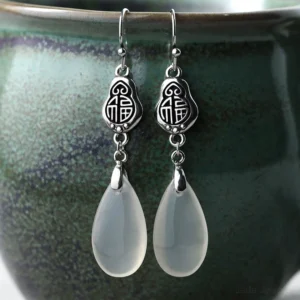 Fu character chalcedony dangle earrings with 925 sterling silver posts displayed on ceramic jar, front close-up view showing embossed Fu symbol and milky white teardrop stone