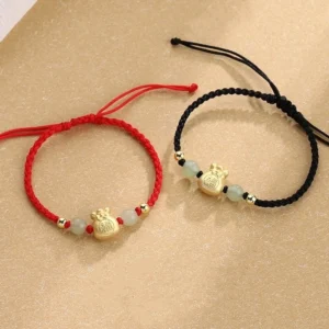 Fu character jade prosperity braided bracelet flat lay showing red and black rope options with gold money bag charm and natural jade beads on warm neutral background