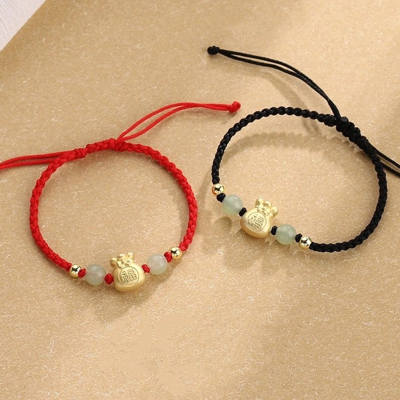 Fu character jade prosperity braided bracelet flat lay showing red and black rope options with gold money bag charm and natural jade beads on warm neutral background