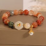 Fu Lu Shou white jade crystal bracelet with pearl pendant displayed in luxury linen jewelry box, flat lay view showing red, yellow, green quartz and white jade beads