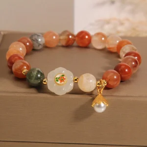 Fu Lu Shou white jade crystal bracelet with pearl pendant displayed in luxury linen jewelry box, flat lay view showing red, yellow, green quartz and white jade beads