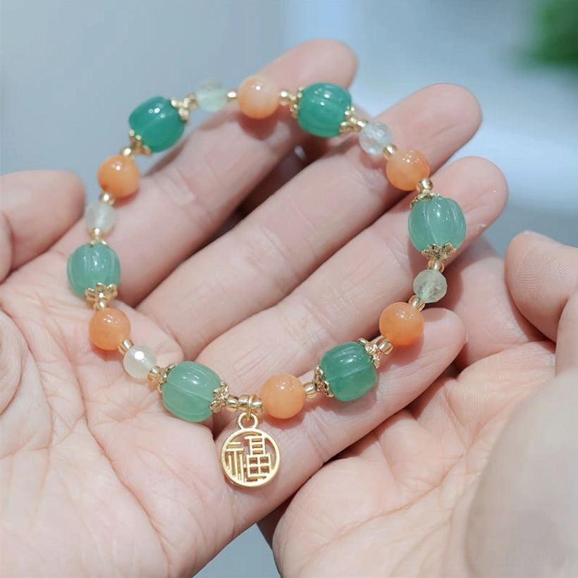 Golden Silk Jade Fu character pumpkin bead bracelet displayed on two palms, showing mixed gemstone beads with gold-toned Fu charm pendant