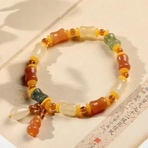 Handcrafted Golden Jade Bracelet with Gourd Charm - Flat lay on antique calligraphy paper showing full elastic band design