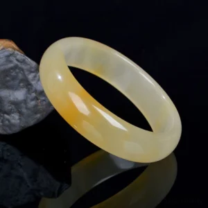 Golden Silk Jade bangle bracelet with warm yellow-white gradient, polished smooth finish displayed on reflective surface
