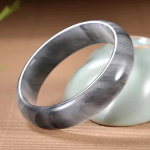 Two matching golden silk jade bangles with distinctive ink-wash marbled patterns, displayed together on decorative table setting