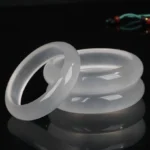 Multiple translucent white golden silk jade bangles displayed in three-quarter view on dark reflective studio background, showcasing smooth polished finish